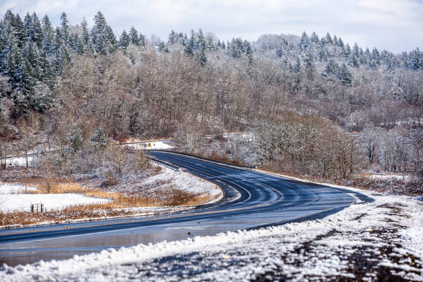 Winter landscape with winding road and hills with snow-covered trees, meadows and road shoulders and mountains hidden in the hanging clouds in the Columbia River Gorge National Recreation Reserve