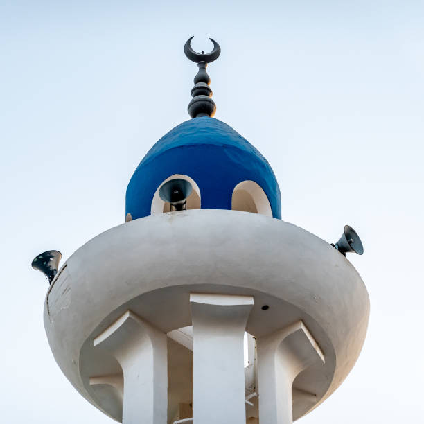 white and blue painted tip of a minaret with loudspeakers and a bronze crescent moon on the side - prayer call imagens e fotografias de stock