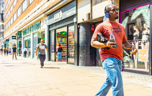 Crowds of shoppers on Regent Street in Central London, UK in the summer of 2018. In the foreground is a young fashionable black man wearing headphones and carrying a drink.