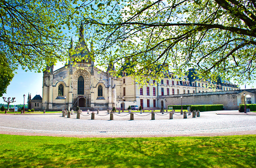 Notre-Dame holy chapel near castle of the Dukes of La Trémoïlle in Thouars, France. Warm spring morning, vibrant blue sky with clouds, green lawn, calm atmosphere. Front facade