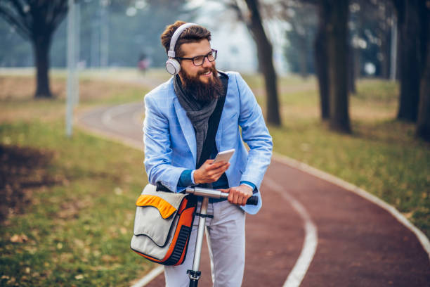 istock Young businessman with a beard smiling on kick scooter 1129573656