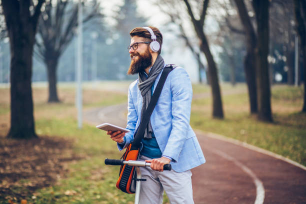 istock Young businessman with a beard smiling on kick scooter 1129573752