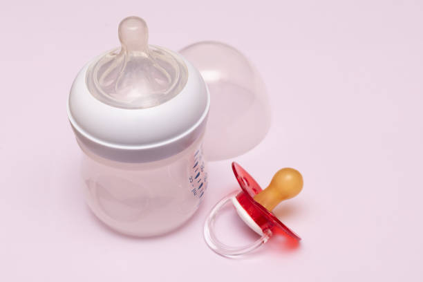Baby bottle and pacifier on pink background.