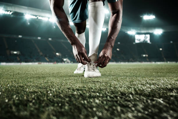 The soccer player kicking the ball at stadium Soccer player football player lace up boots at the stadium. The stadium is made in 3D.. football player lace up boots football boot stock pictures, royalty-free photos & images