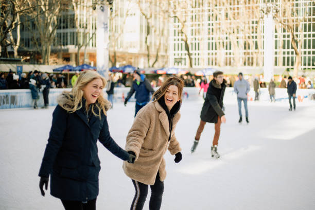 Having Fun on the Ice Rink A front-view shot of two mid-adult women ice skating together in an ice rink in New York City, they are wearing warm clothing, holding hands and laughing together. ice skating stock pictures, royalty-free photos & images