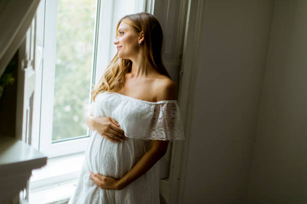 istock Young pregnant woman standing by the window 1129580876