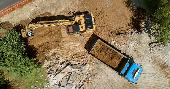 Excavator excavating soil at construction site and loading it onto truck.