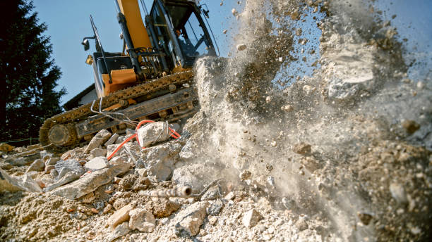 Grapples on excavator crushing large concrete block in air.