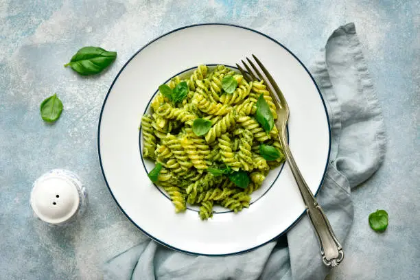 Fusilli pasta with basil pesto on a plate over light blue slate, stone or concrete background. Top view with copy space.