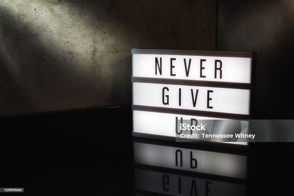 Never give up motivational message on a light box Never give up motivational message on a light box in a cinematic moody background Conquering Adversity Stock Photo