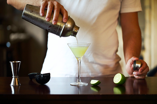 Bartender at work, preparing cocktails. Pouring martini to cocktail glass. Service and beverages concept