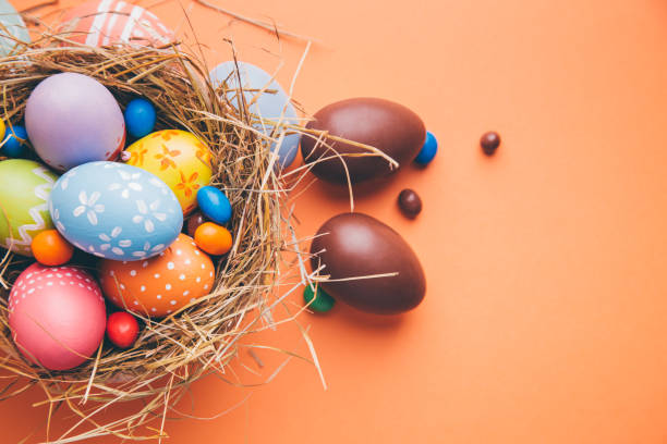 istock Colorful easter eggs with chocolate and candies in a nest on a orange background 1129603104