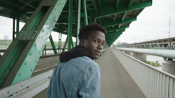 African man on walk. looking away. Steel construction of bridge.