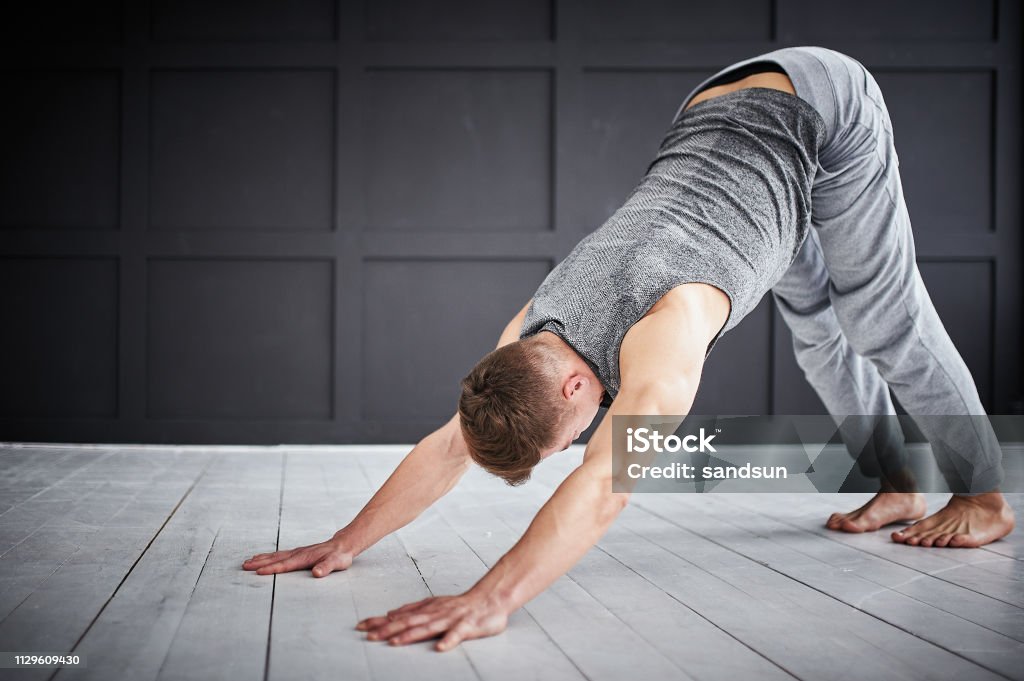 Young strong man practices yoga at the yoga studio Young strong man practices yoga at the yoga studio. Downward Facing Dog Position Stock Photo