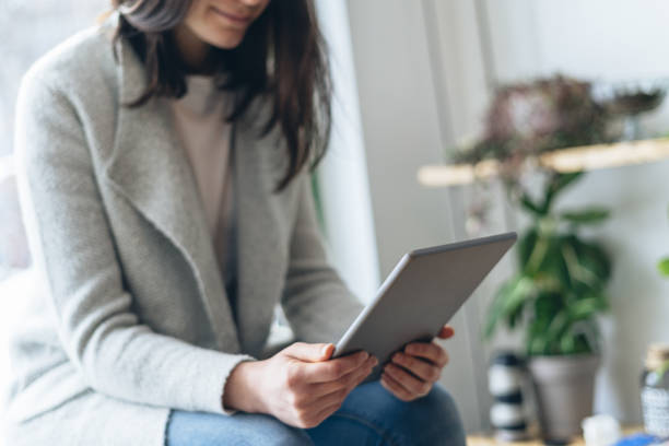 istock Profile side view cropped photo of unrecognizable lady sitting inside restaurant space. She holding tablet in hands and looking at display 1129610471