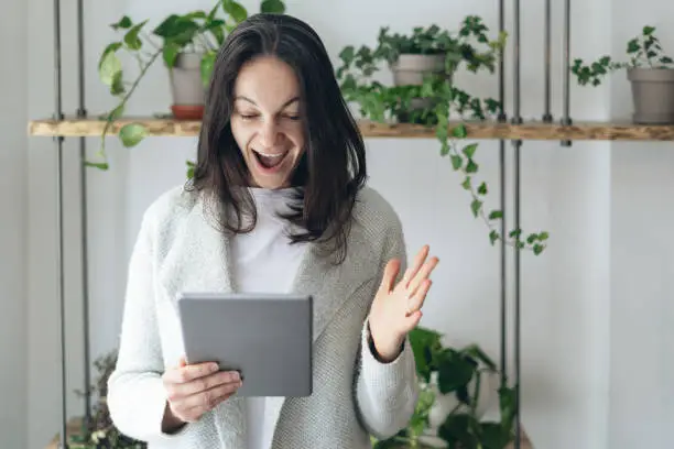 Search and found concept. Photo of exited lady with tablet in hands standing inside co working or restaurant space. She making happy face with wide open mouth