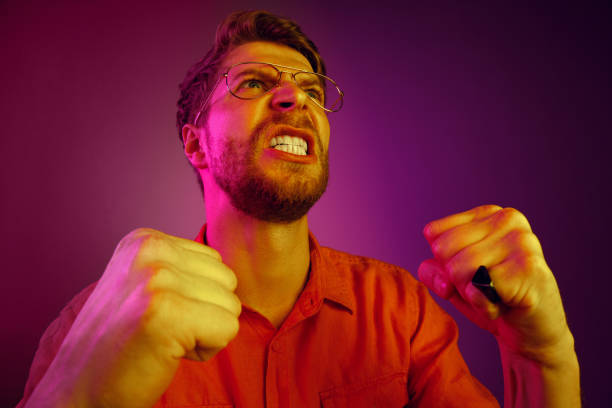 istock The young emotional angry man screaming on pink studio background 1129613526
