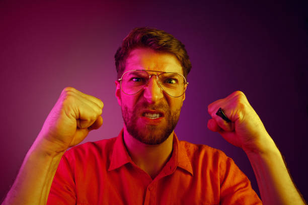 istock The young emotional angry man screaming on pink studio background 1129613532