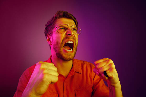 istock The young emotional angry man screaming on pink studio background 1129613533