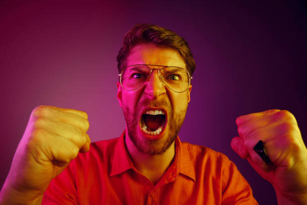 istock The young emotional angry man screaming on pink studio background 1129613539