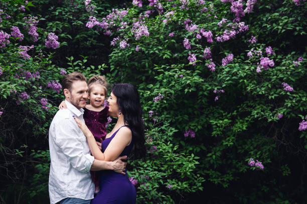 cheerful happy family hugging near lilac flowering bushes cheerful happy family hugging near lilac flowering bushes. holding child flower april stock pictures, royalty-free photos & images