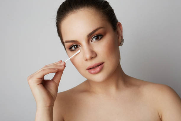 istock Handsome girl refreshing skin face with white cotton buds over gray studio background.Model with light nude make-up.Healthcare skin makeup concept. 1129617854
