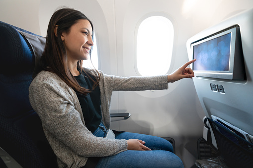 Portrait of a happy Latin American woman traveling by plane and watching onboard entertainment - travel concepts. **DESIGN ON SCREEN WAS MADE FROM SCRATCH BY US**