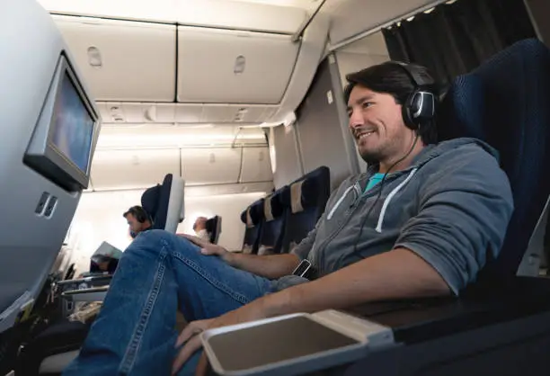 Portrait of a happy man traveling by plane watching in-flight entertainment using earphones