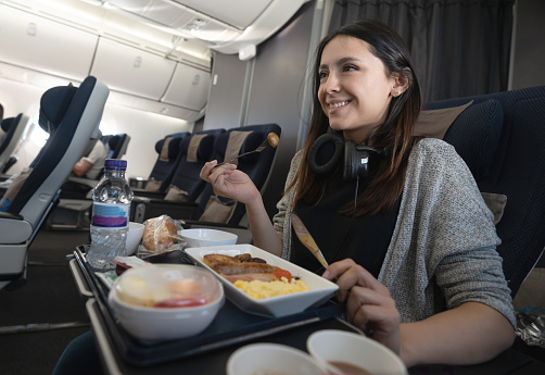 Portrait of a happy woman traveling by plane and eating food onboard - travel concepts