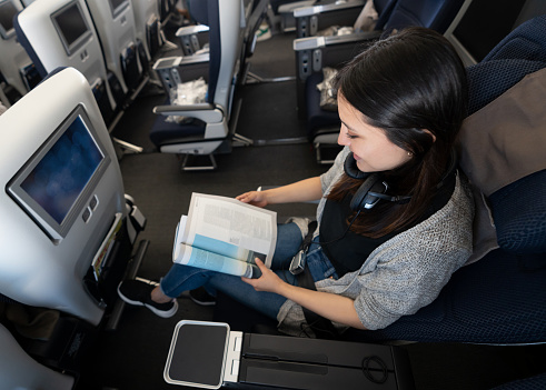 Happy young woman traveling by plane and reading a magazine onboard - travel concepts