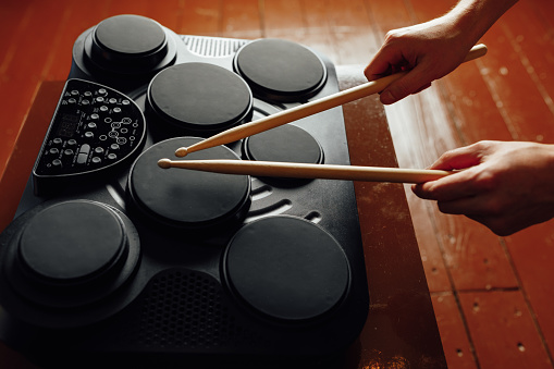 hands playing on portable electronic drums, brown background, close-up view