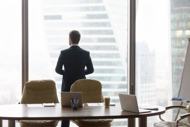 istock Rear view at successful businessman standing back in modern office 1129629289
