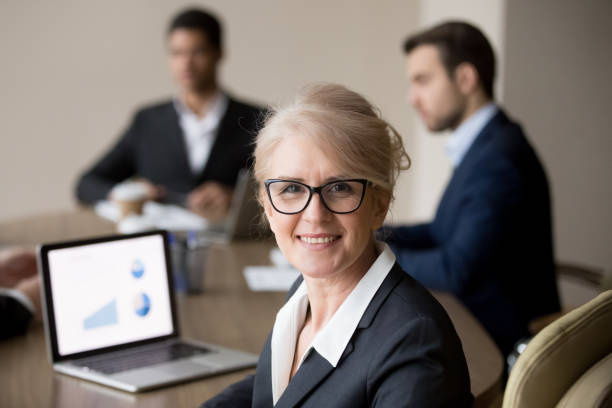 femme d’affaires d’âge mûr heureux dans des verres en posant à la réunion de l’équipe office - info board photos et images de collection