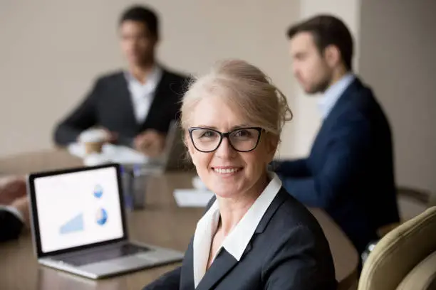 Photo of Happy middle-aged businesswoman in glasses posing at team office meeting