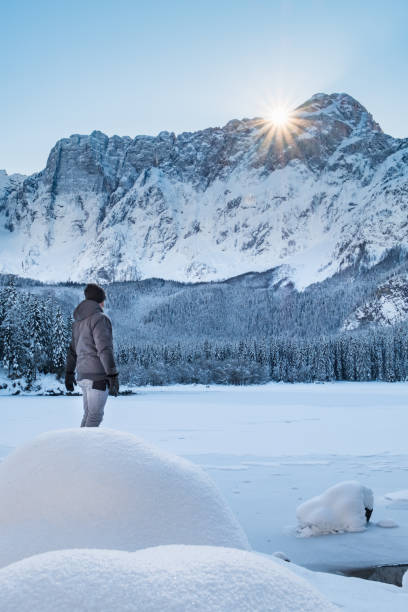 istock Man standing on snow covert lake looking to mountain sunbeams 1129635108