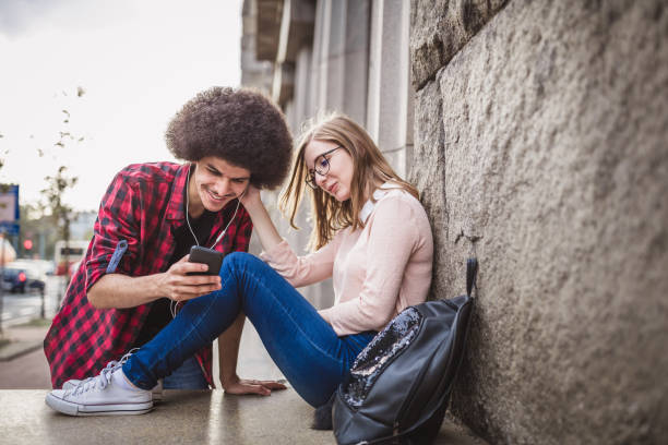 istock Young couple, sitting on a sidewalk wall, browsing the internet on a mobile phone 1129635574