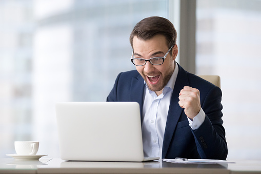 Excited businessman in suit feeling winner celebrating online victory business success watching game at work looking at laptop, happy male executive ceo received good news, winning bet bid results