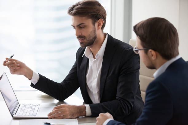 istock Serious businessman manager talking with client pointing at laptop 1129638550