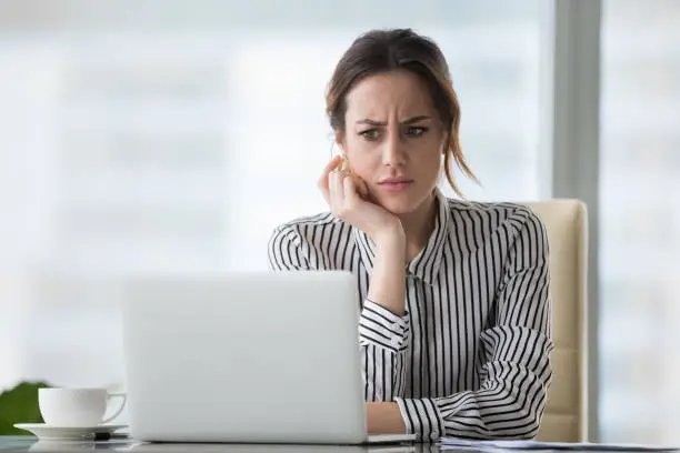 Photo of Confused businesswoman annoyed by online problem looking at laptop