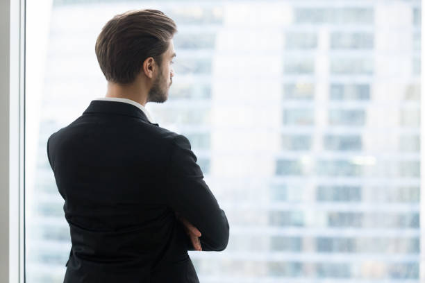 istock Rear view at businessman looking through window at modern city 1129638611