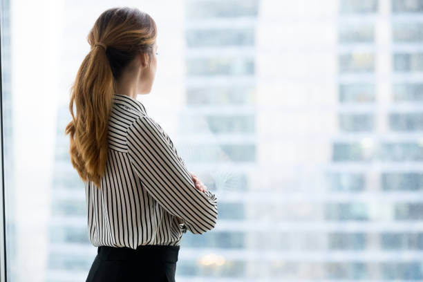 istock Rear view at confident rich businesswoman looking forward through window 1129638618