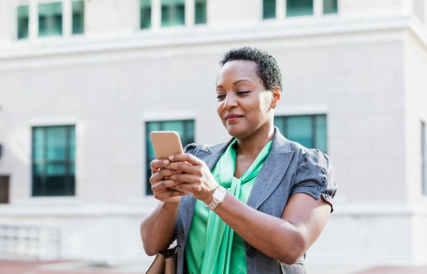 mature african-american woman in city texting - women common 40s candid imagens e fotografias de stock