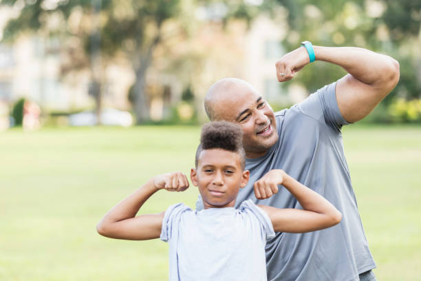 padre e figlio flettevano giocosamente i muscoli - flexing muscles child little boys bicep foto e immagini stock