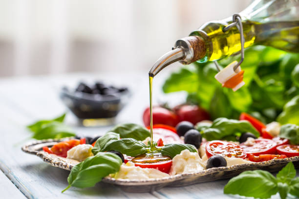 versando olio d'oliva sull'insalata caprese. pasto sano italiano o mediterraneo - salad food caprese salad gourmet foto e immagini stock