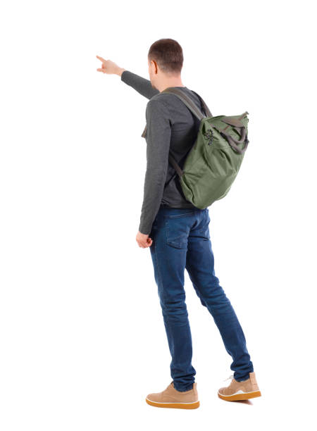 istock Back view of a man with a green backpack pointing forward. 1129645642