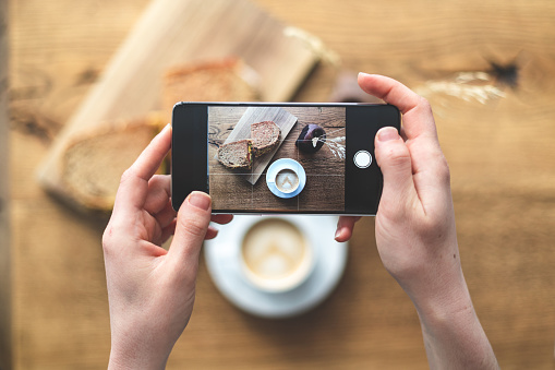 High angle above top view and cropped photo of woman with portable telephone equipment in hands. She making photo for social network standing inside loft interior space in restaurant