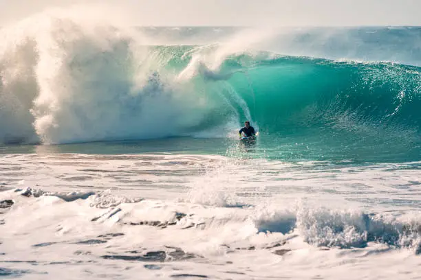 man surfing the barrel of a perfect wave that breaks with a power and energy, the sunlight reflects on the turquoise surface of the sea and in the huge pile of foam, the wind lifts up plumes of water