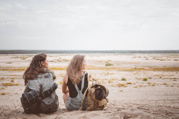 istock Young female hikers sitting with backpacks on sand 1129663404