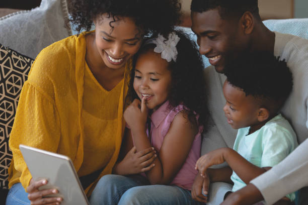 istock Happy African American parents with their cute children using digital tablet on sofa 1129665081