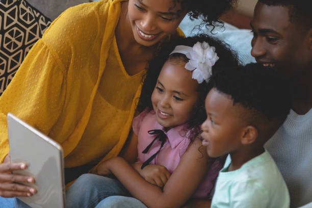 istock Happy African American parents with their cute children using digital tablet on sofa 1129665112